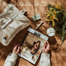 Lade das Bild in den Galerie-Viewer, Topshot von weißem Scout Backpack und Hand die in stylischem Magazin blättert