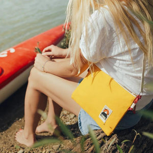 Frau im Sommeroutfit am Wasser mit gelber Ykra Side Pouch in gelb