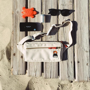 Ykra Fanny Pack in weiß auf Holzsteg am Strand daneben Sonnenbrille Buddelförmchen Fotoapparat 