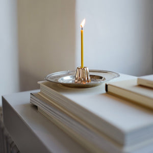 Bronze Kerzenhalter von Ovo mit brennender dünner Kerze auf silbernen Teller stehend auf gestapelten Büchern