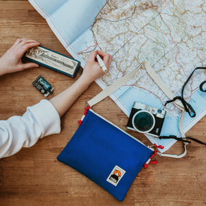 Side Pouch in blau liegt neben Landkarte und Fotokamera