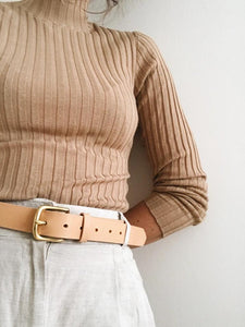 Frau mit heller Stoffhose und geripptem Rollkragenpulli trägt natürlich gegerbten SJAELV Ledergürtel in der Farbe Nude